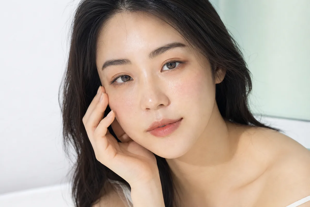 Woman with clear, calm, even toned skin resting her fingertips on her cheekbone