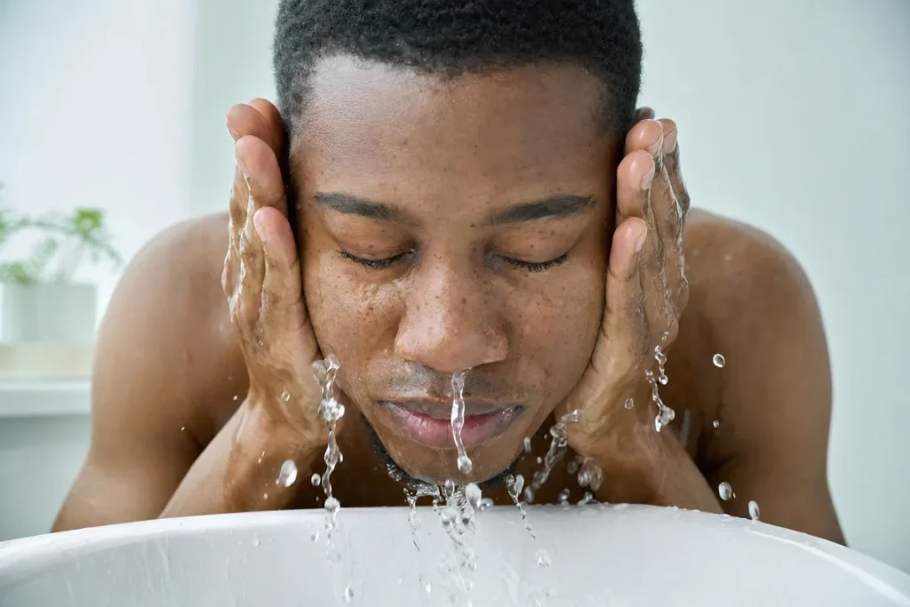 Young man splashing water on his face, clear skin with natural pores across the nose