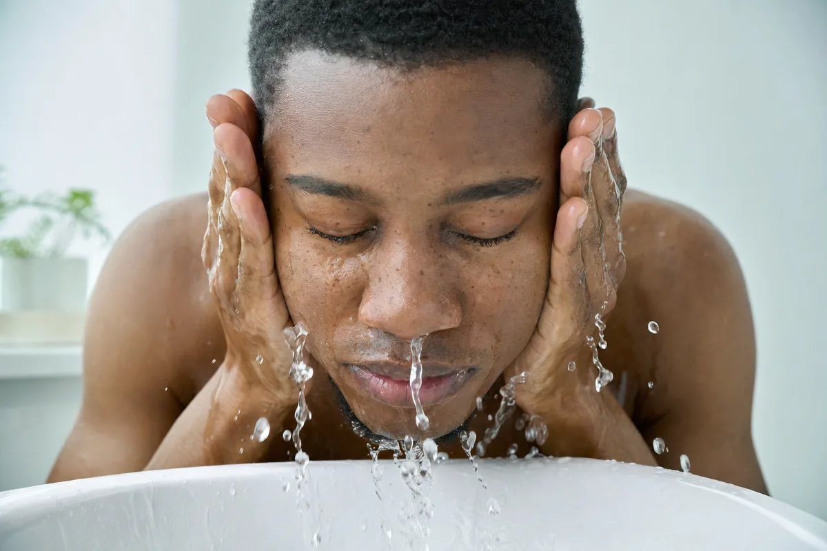 Young man splashing water on his face, clear skin with natural pores across the nose