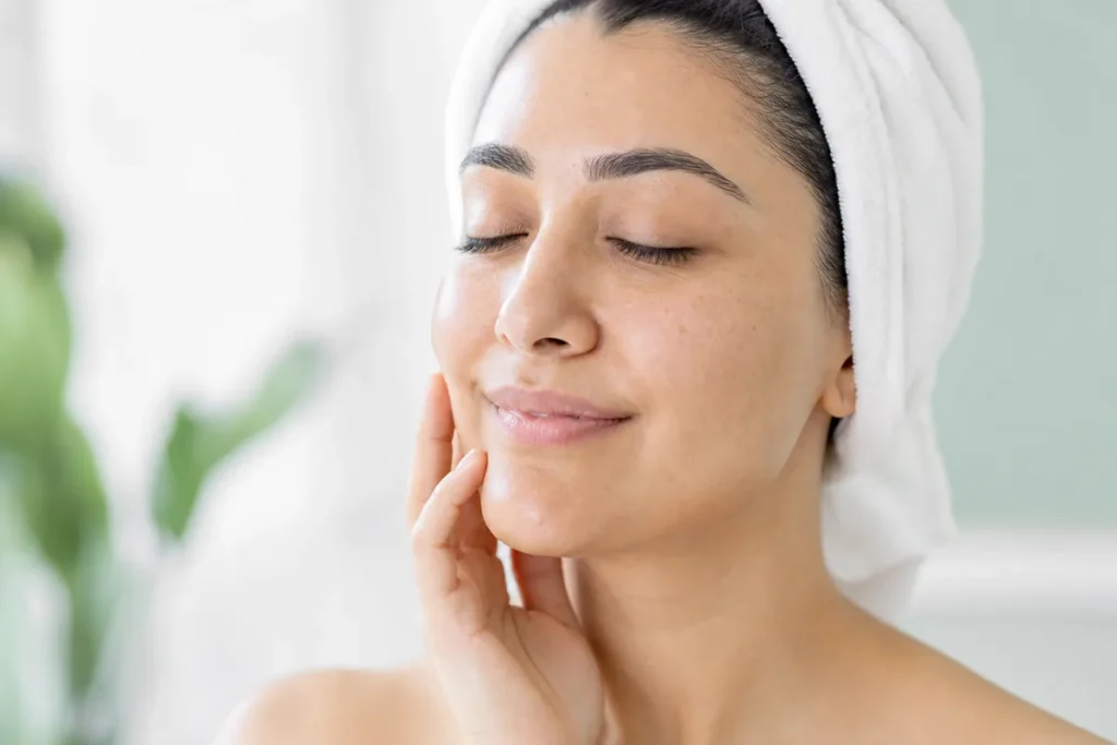 Woman with a white towel headband and freshly hydrated, glowing skin after a facial